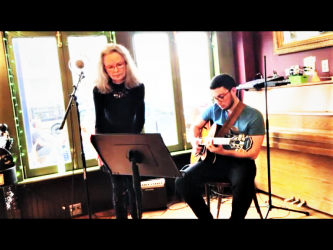 Dr. Nancy Mroczek performing with a man on guitar to her right.
