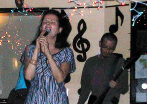 Dr. Nancy Mroczek singing with a man in the background on guitar.